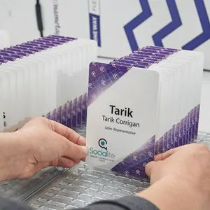 Badges Événementiels Imprimés Prêts à Distribuer – IDCGO Mains organisant une pile de badges événementiels imprimés au design violet et blanc, avec noms des participants et logos d’entreprise.