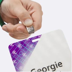 Fixation d’un Clip sur un Badge Événementiel – IDCGO Gros plan d’une main fixant un clip métallique sur un badge événementiel imprimé au design violet et blanc.