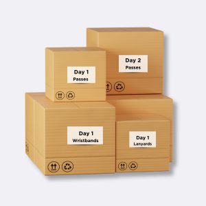 Cartons d’Expédition Étiquetés pour Événements – IDCGO Pile de cartons d’expédition étiquetés et organisés par jour d’événement, contenant bracelets, lanyards et pass